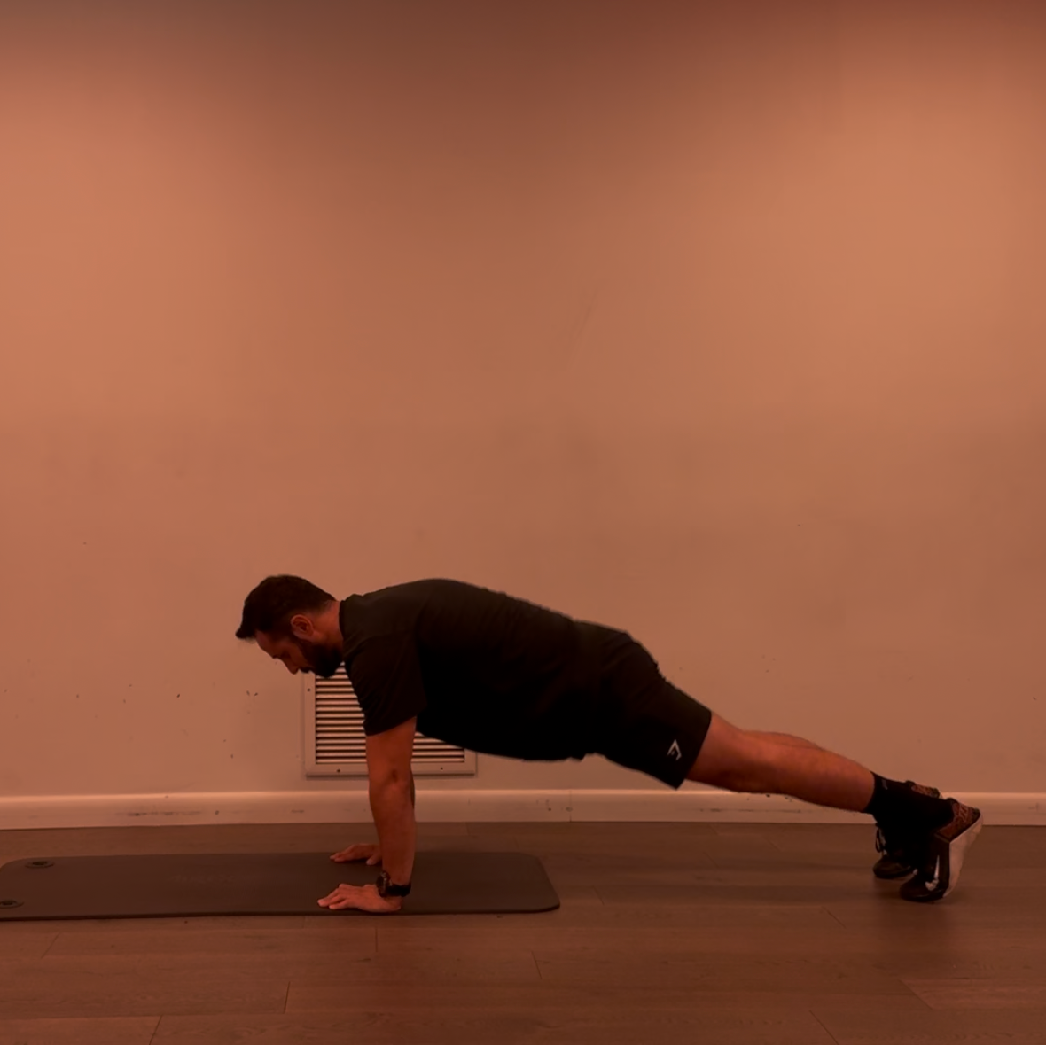 Person performing a push-up on a mat against a plain wall.